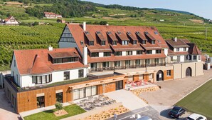 Un hotel con diversi piani, un cortile con posti a sedere all'aperto e un vigneto sullo sfondo.