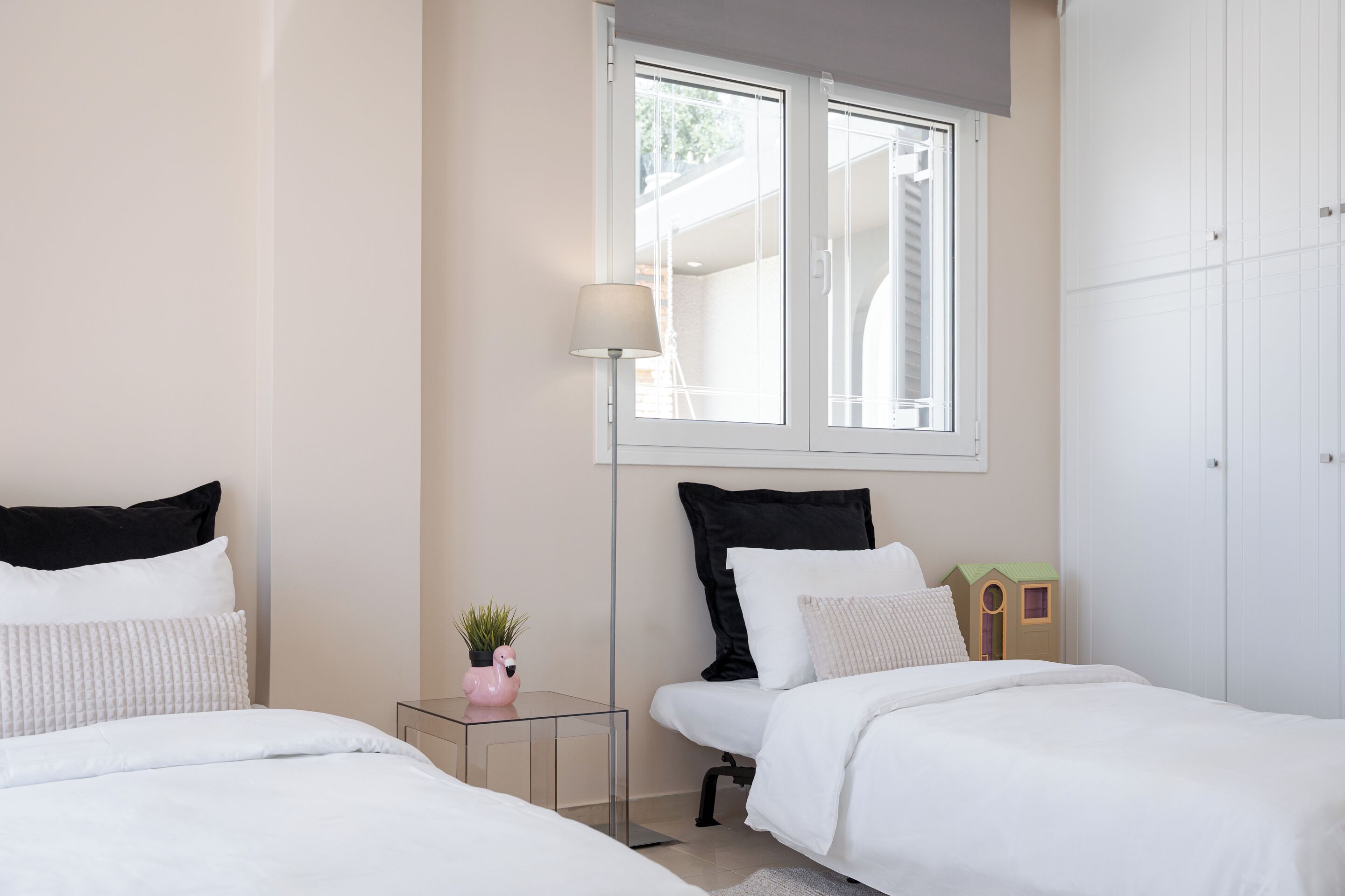 Une chambre avec deux lits, une fenêtre, une lampe et une petite plante.