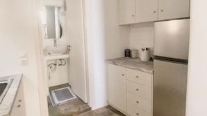 A compact kitchen with white cabinets, a built-in oven, and a stone-patterned floor. - Simousi Studio 1 sea View on the Beach (Kithnos)
