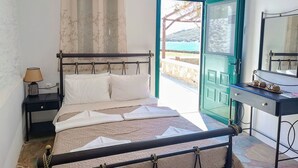 A bedroom with a bed, bedside table, lamp, and a view of the sea through an open door. - Simousi Studio 1 sea View on the Beach (Kithnos)