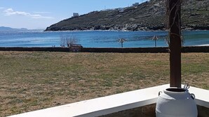 A coastal view with a grassy area, a white vase, and a rocky hillside in the background. - Simousi Studio 1 sea View on the Beach (Kithnos)