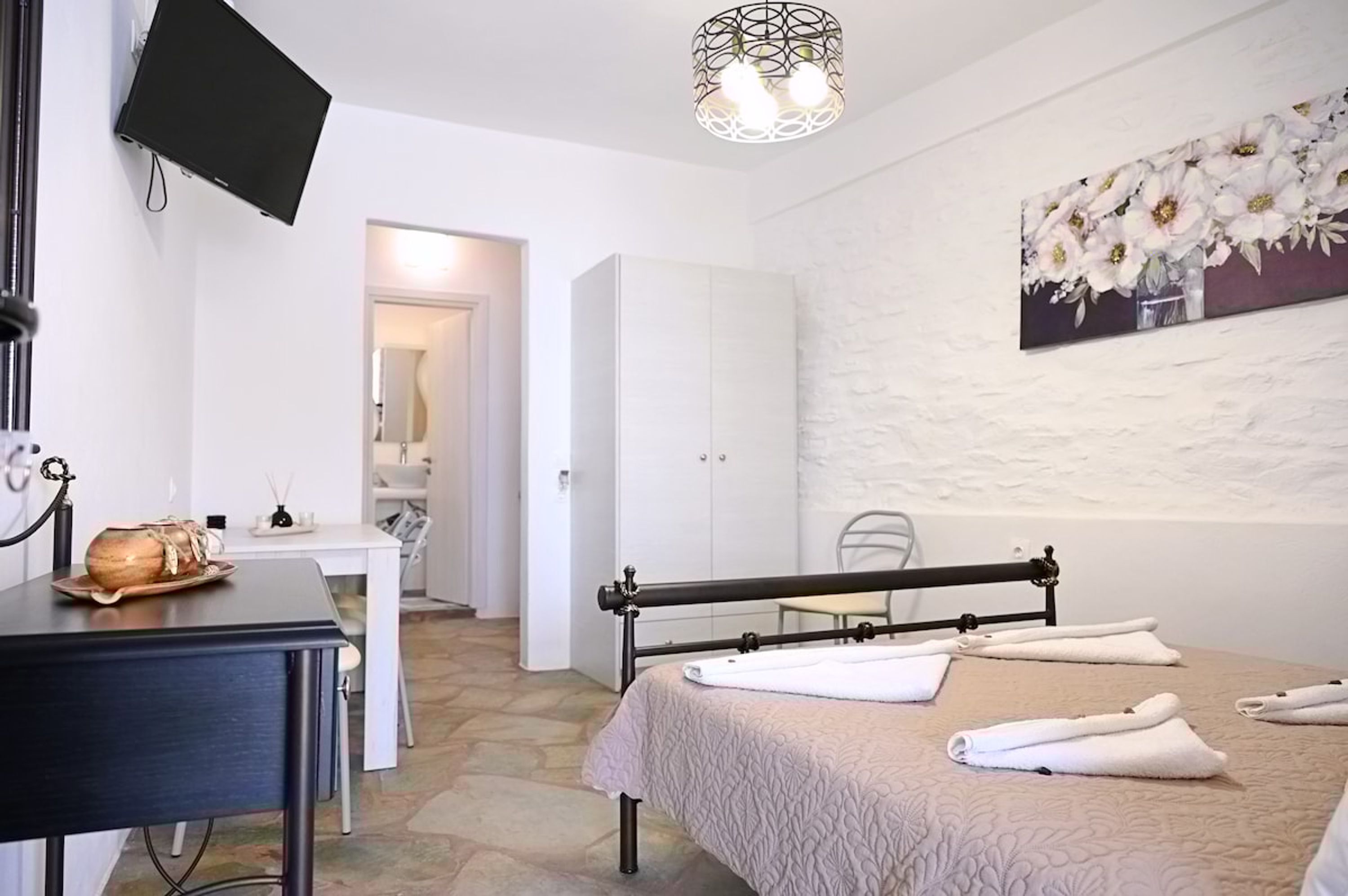 Una habitación de hotel con una cama, un escritorio, una silla, un televisor y un cuadro en la pared.