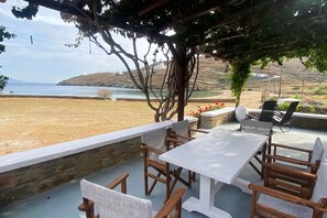An outdoor patio with a table and chairs, overlooking a beach and hills.