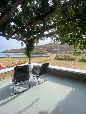 An outdoor seating area with two black metal chairs and a white vase, overlooking a coastal landscape with hills and a body of water.