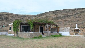 Ein Steinhaus mit Garten, einer Steinmauer und einer Hügelkulisse im Hintergrund.