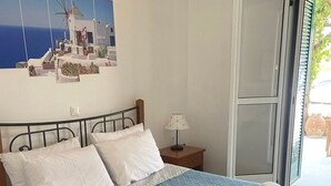 Ein ordentlich bezogenes Bett mit weißen Laken und einer blauen Steude, eine Nachttischlampe und ein Fenster mit Blick auf Grün.