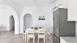 Een moderne keuken met witte kasten, een roestvrijstalen koelkast en een eethoek met een witte tafel en stoelen.