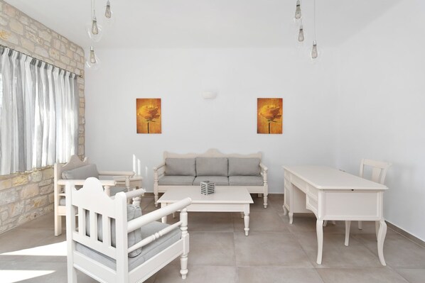 A room with a stone wall, white furniture, a sofa, a table, and two paintings.