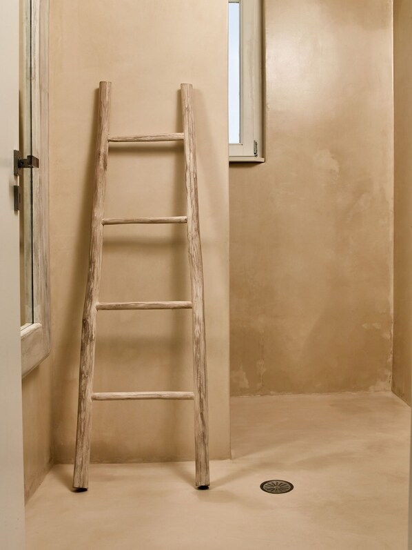 Une échelle en bois est appuyée contre un mur beige dans une pièce qui comporte une petite fenêtre et une porte.