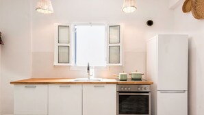A kitchen with white cabinets, a wooden countertop, a stainless steel oven, a white refrigerator, and a window with white shutters. - Menta II in Naousa With Free Parking Paros (Paros)