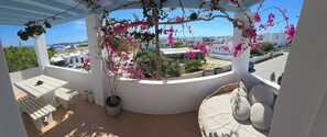 A balcony with a white table and chairs, a wicker basket, and a bed with pillows. - Menta I in the Heart of Naousa Free Parking Paros (Paros)