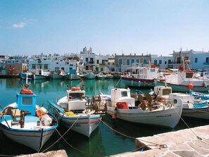 A harbor with multiple boats docked, surrounded by buildings with a consistent architectural style. - Menta I in the Heart of Naousa Free Parking Paros (Paros)