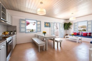 A modern kitchen with white cabinets, a built-in oven, and a dining area with a white table and benches. - Menta I in the Heart of Naousa Free Parking Paros (Paros)