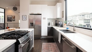 A modern kitchen with white cabinets, stainless steel appliances, and a large window offering a view of residential buildings. - Space City - Prof. Design, Game Room, King BD (Houston)