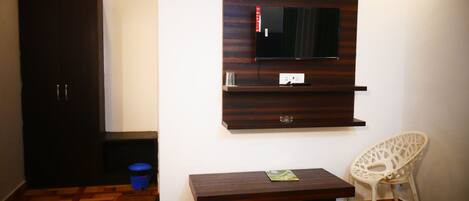 A bedroom with a bed, a wooden desk, a chair, a wardrobe, and a TV mounted on the wall.