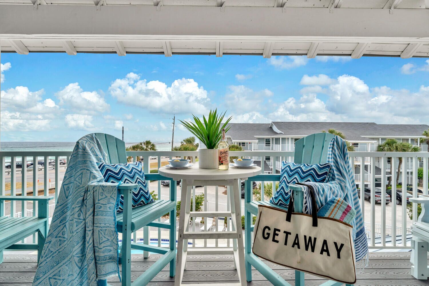A balcony with two turquoise chairs, a small table with a potted plant and a bottle, and a 'GETAWAY' bag.