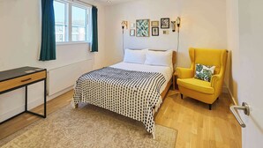 Een slaapkamer met een bed, een stoel, een bureau en een raam met gordijnen.
