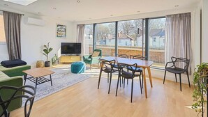 Een moderne woonkamer met een eethoek, grote ramen en een televisie.