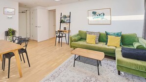 Een moderne woonkamer met een groene bank, een houten salontafel en een eethoek met een houten tafel en stoelen.