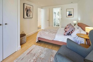 Een moderne hotelkamer met een groot bed, een grijze fauteuil, een klein tafeltje en kunst aan de wanden.