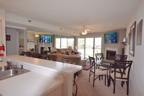 A modern kitchen with a central island, a dining area with a glass table and chairs, a living room with a sofa and a fireplace, and large windows offering a view. - Waterfront -Wifi -2 Pools/Sandy Beach/Great Location- Grill- Boat slip available (Osage Beach)