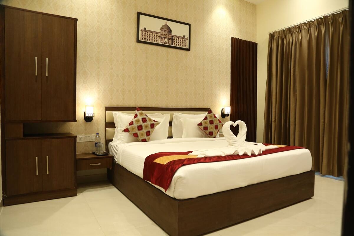 A hotel room with a large bed, wooden wardrobe, bedside table, and a framed picture on the wall.