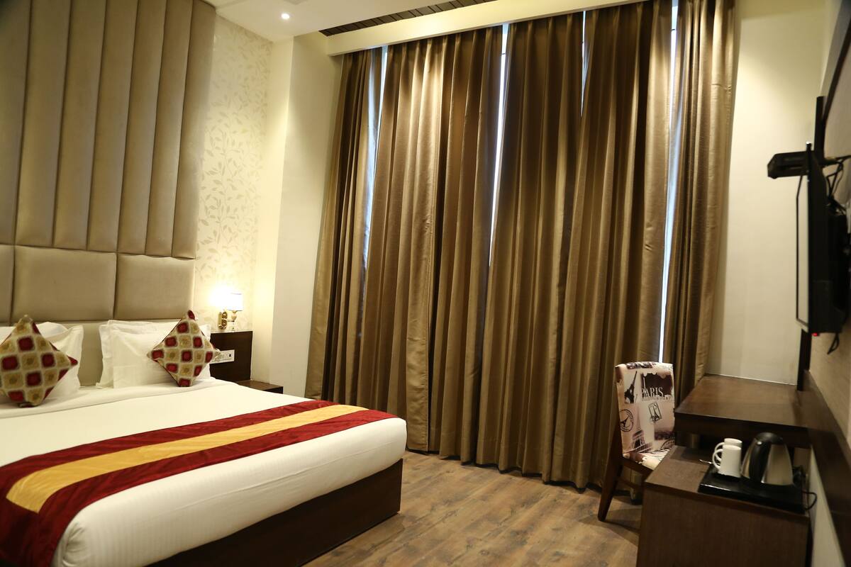A hotel room with a large bed, a desk, a chair, and a window with curtains.