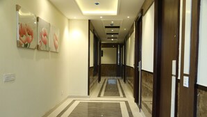 A hotel hallway with a marble floor, wooden doors, and framed artwork on the walls. - Hotel Blue Sapphire (Dera Bassi)