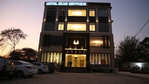 A two-story hotel with a modern facade, a prominent entrance with a lit sign, and a parking area with several cars. - Hotel Blue Sapphire (Dera Bassi)