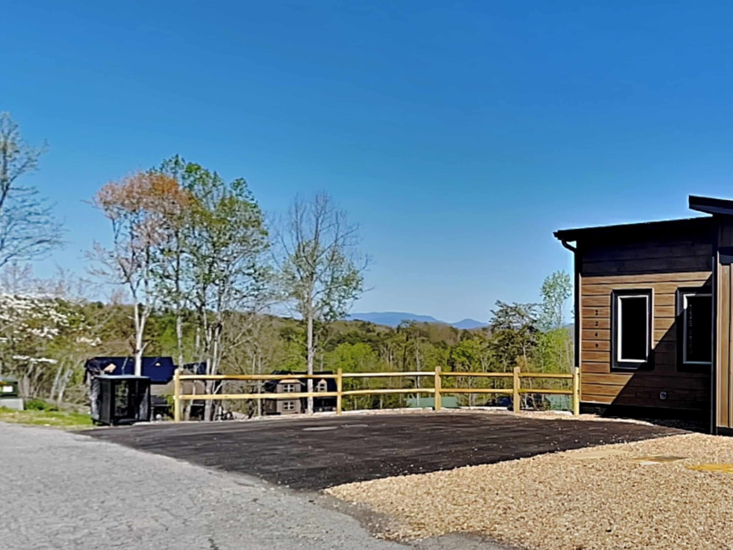 Une cabane en bois moderne dotée d’une grande terrasse, entourée d’arbres et offrant une vue sur un ciel dégagé.