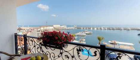 Un balcón con una mesa, una maceta y vistas a un puerto deportivo con barcos y edificios.