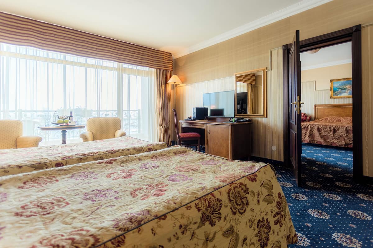 Habitación de hotel con dos camas, un escritorio, una silla, televisión y balcón con vistas.