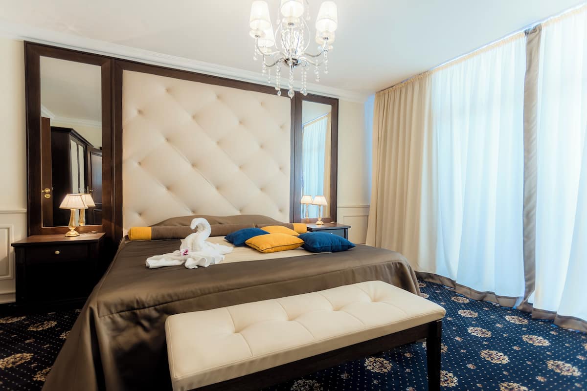 Una habitación de hotel con una cama grande, un banco, una araña y un espejo amplio.