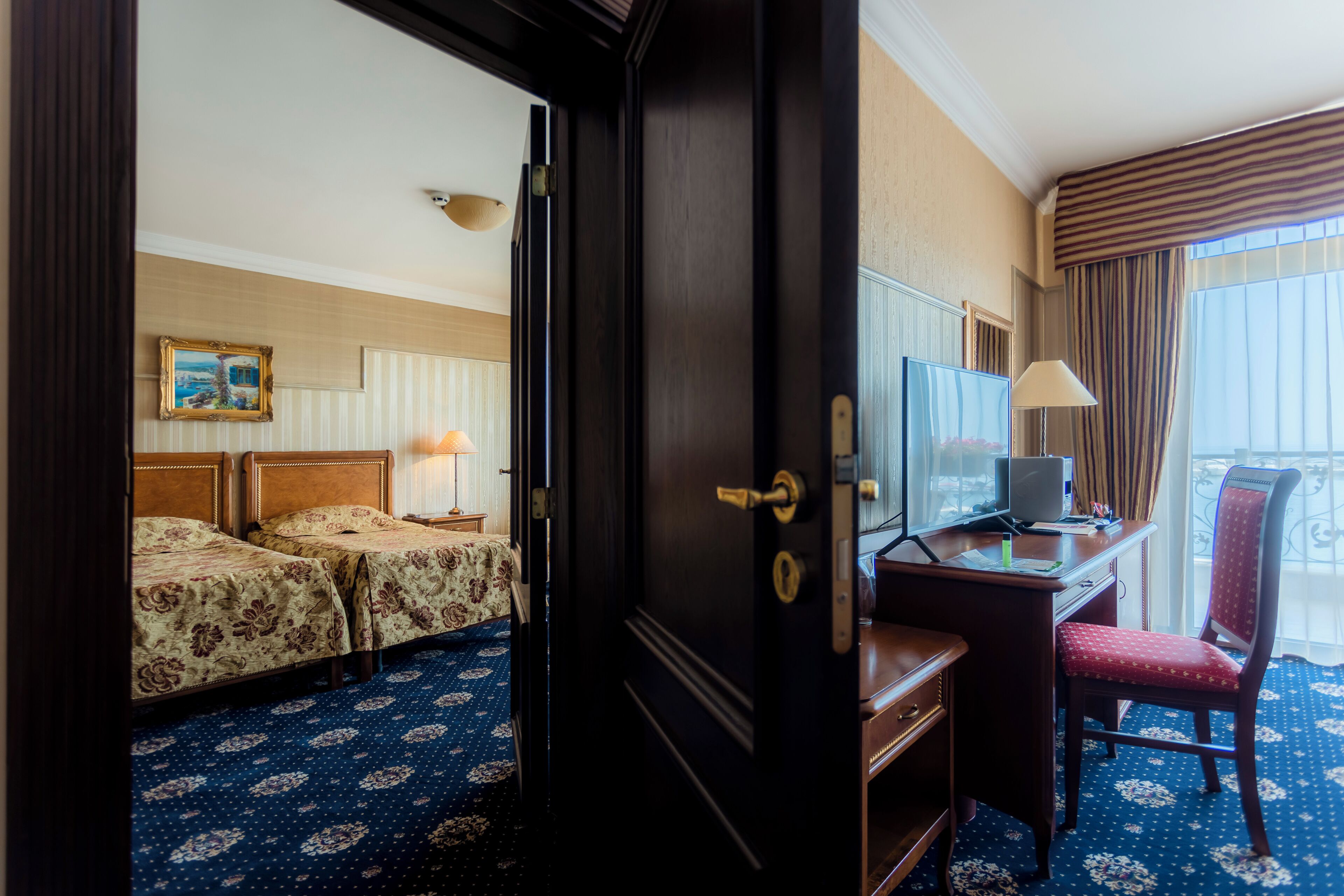 A hotel room with two beds, a desk with a computer, a chair, and a large window with curtains.