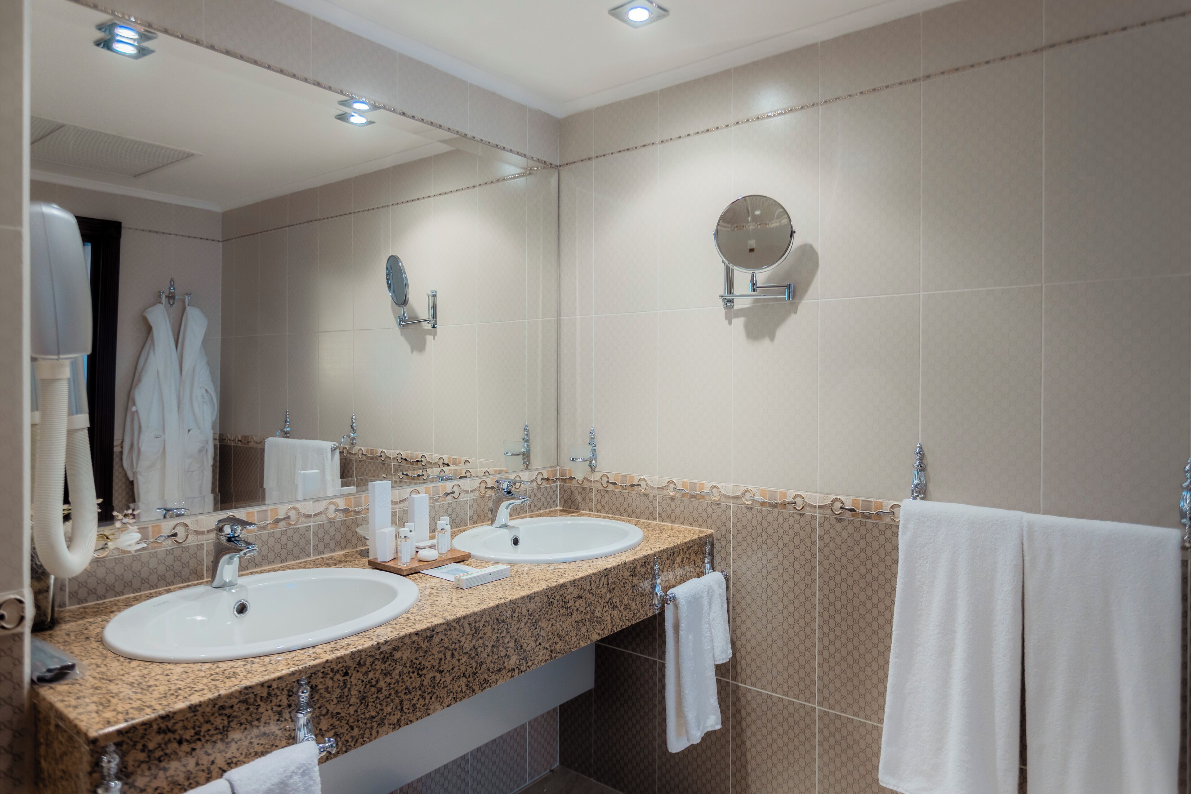 A hotel bathroom with two sinks, a large mirror, and a towel rack.