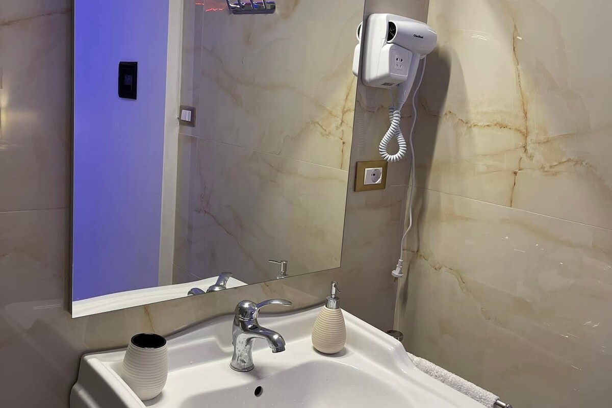 A modern bathroom with a white sink, a mirror, and a hairdryer mounted on the wall.
