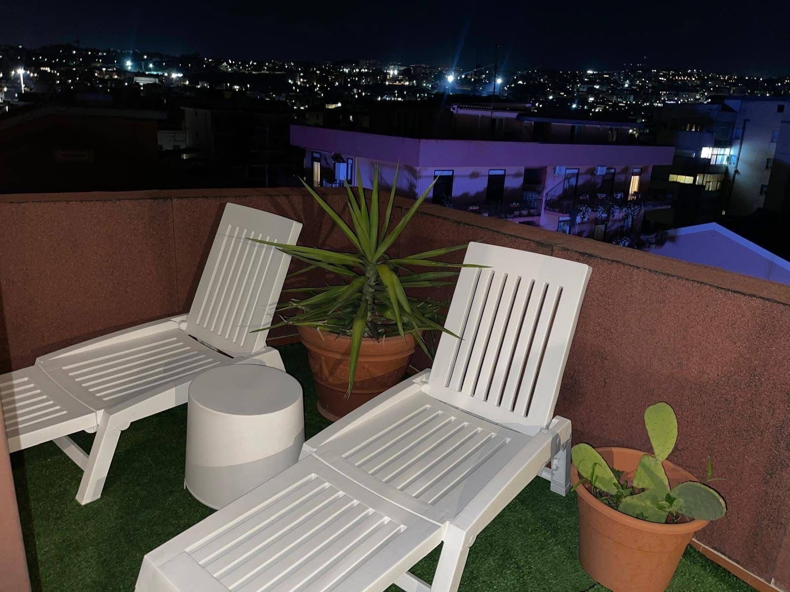 Una terrazza sul tetto con due poltrone bianche, un tavolo bianco rotondo e una pianta in vaso.