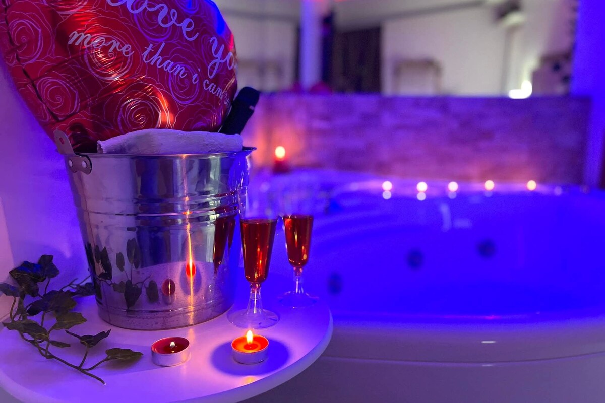 A room with a jacuzzi, a bucket with a towel, and two lit candles on a table.