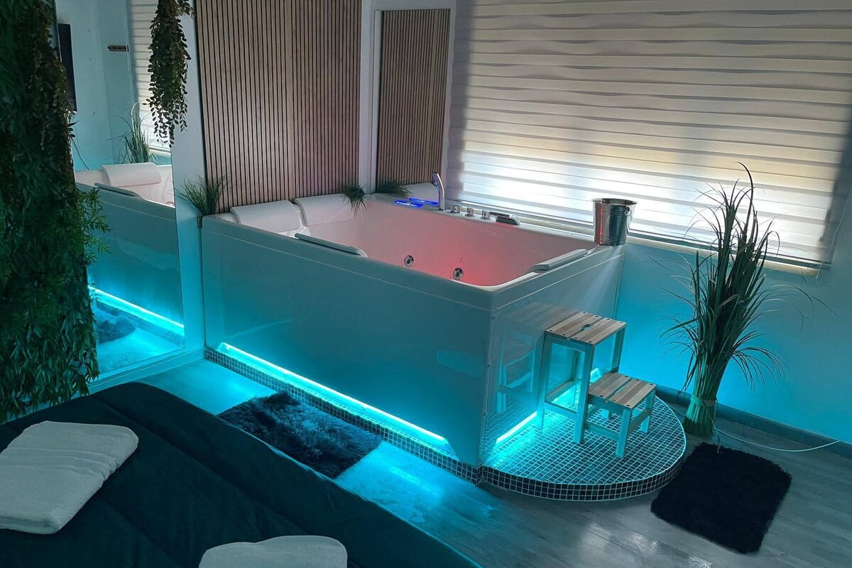 A modern spa room with a hot tub, a wooden bench, and a small table.