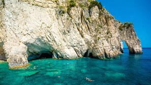 Une falaise côtière surplombant une eau d’un bleu limpide, avec une arche naturelle.