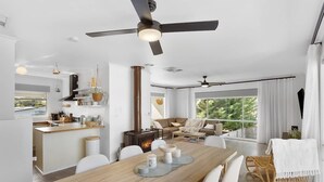 Un interior moderno con comedor, cocina y sala de estar, que cuenta con ventiladores de techo, ventanas amplias y chimenea.