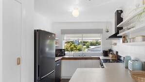 Cocina moderna con refrigerador negro, alacenas blancas, encimera de madera y ventana con vista a vegetación.
