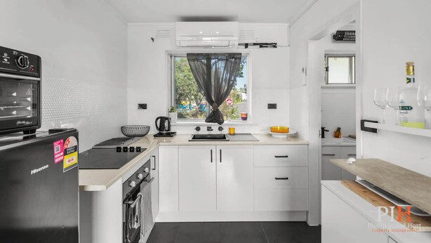 Una cocina moderna con armarios blancos, una cocina por inducción negra, un hervidor y una ventana con vistas al exterior.