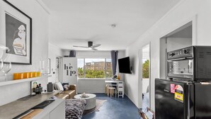 Un espacio habitable compacto con kitchenette, una zona de comedor y una sala de estar con sofá y mesa de centro.