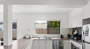 A modern kitchen with white cabinets, stainless steel appliances, and a large window offering a view of the outdoors.