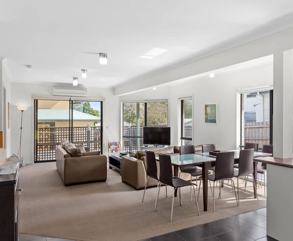 A modern living room with a sofa, dining table, chairs, and a TV.