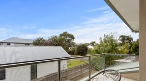 A balcony with a metal railing, a wicker chair, and a view of a residential area with houses and trees.