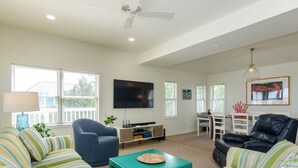 Una sala de estar moderna con televisor de pantalla plana, ventilador de techo y comedor con mesa y sillas.