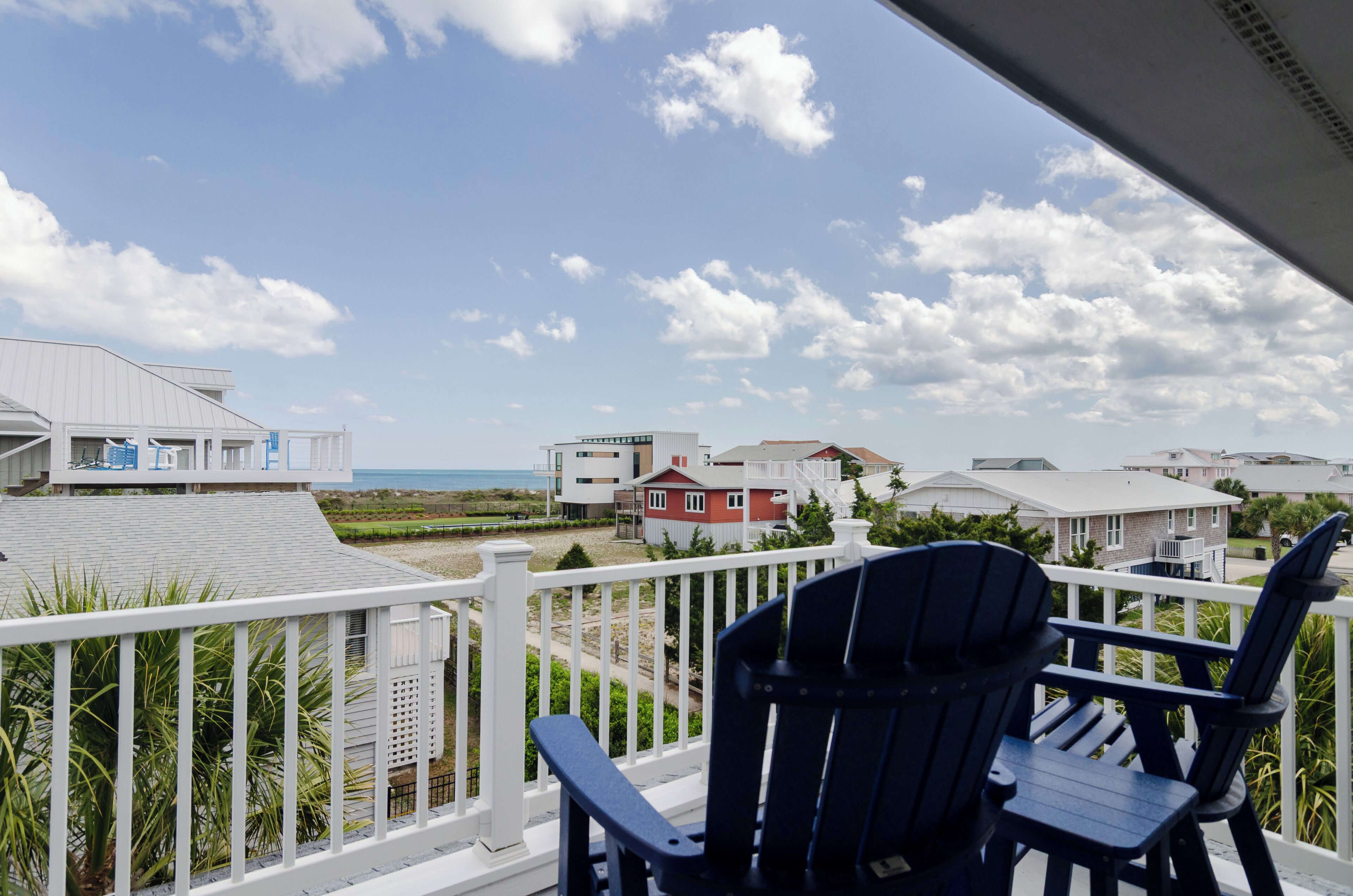 Ein Balkon mit zwei Adirondack-Stühlen mit Blick auf einen Strand und Wohnhäuser.