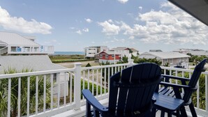 Un balcón con dos sillas Adirondack que da a una playa y edificios residenciales.